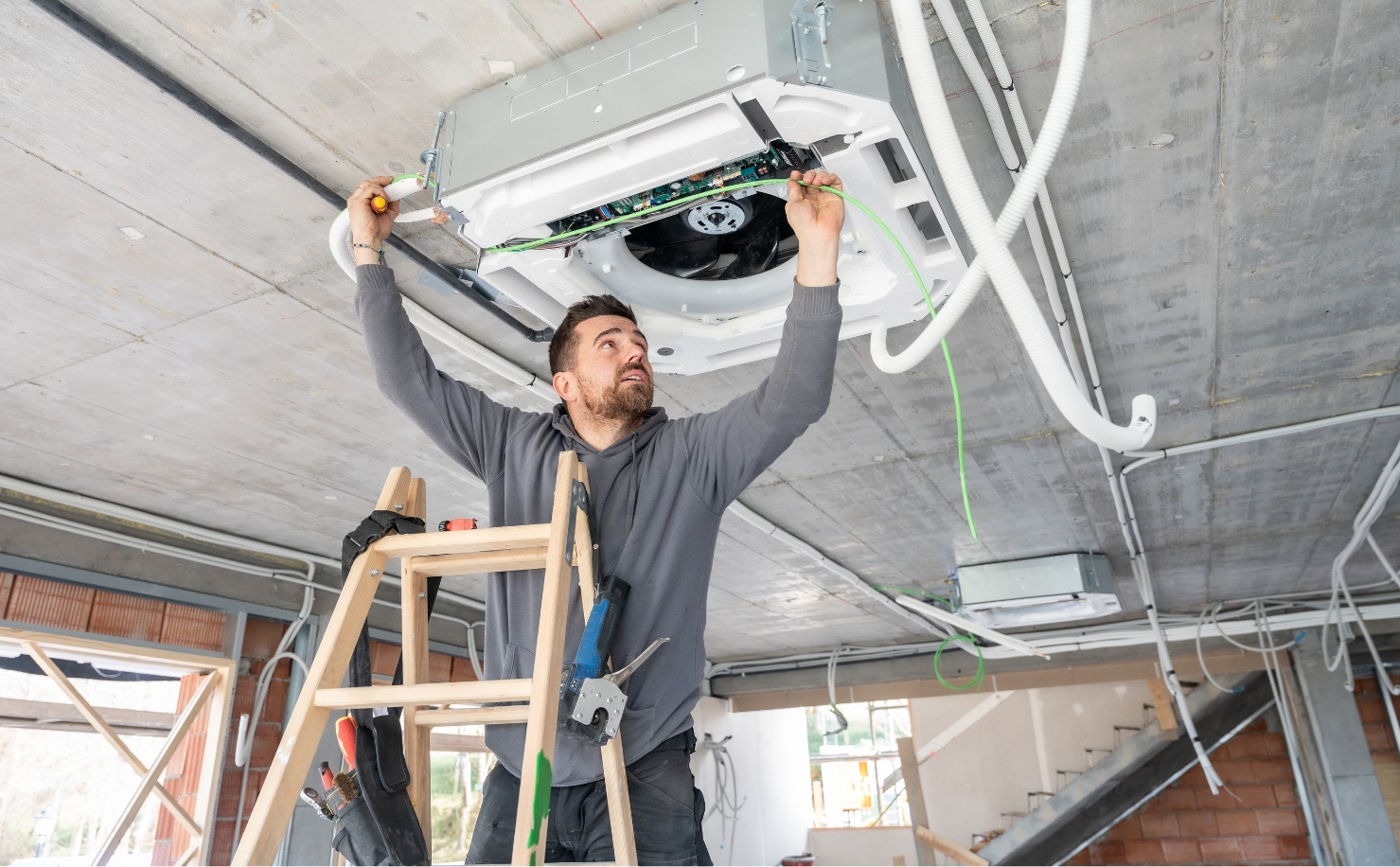 man on ladder fixing air conditioning unit on ceiling
