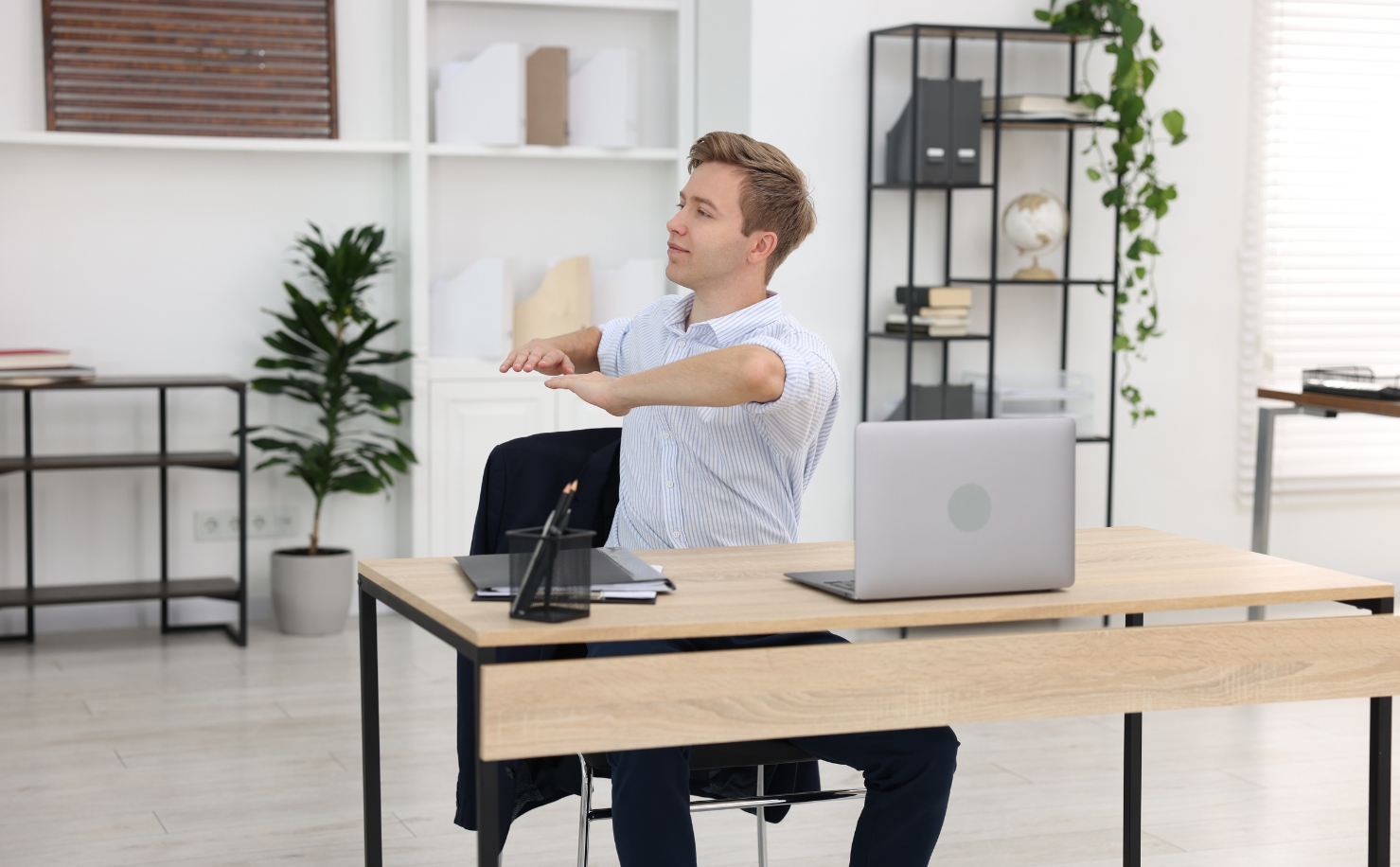 man ssitting and tretching at desk in front of laptop